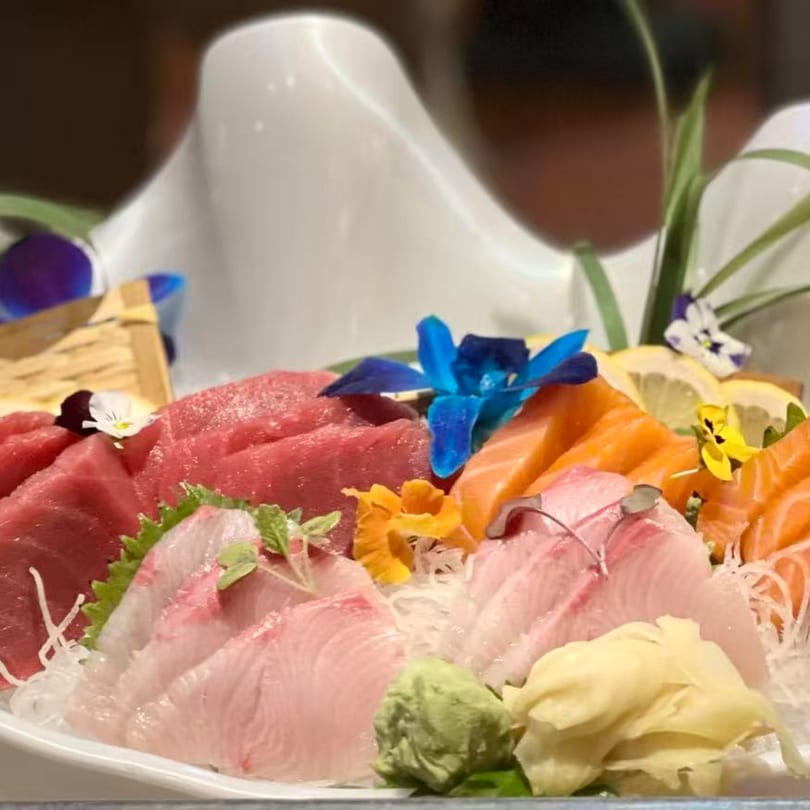 A platter of fresh sashimi, including tuna, salmon, and white fish, garnished with flowers and lemon.
