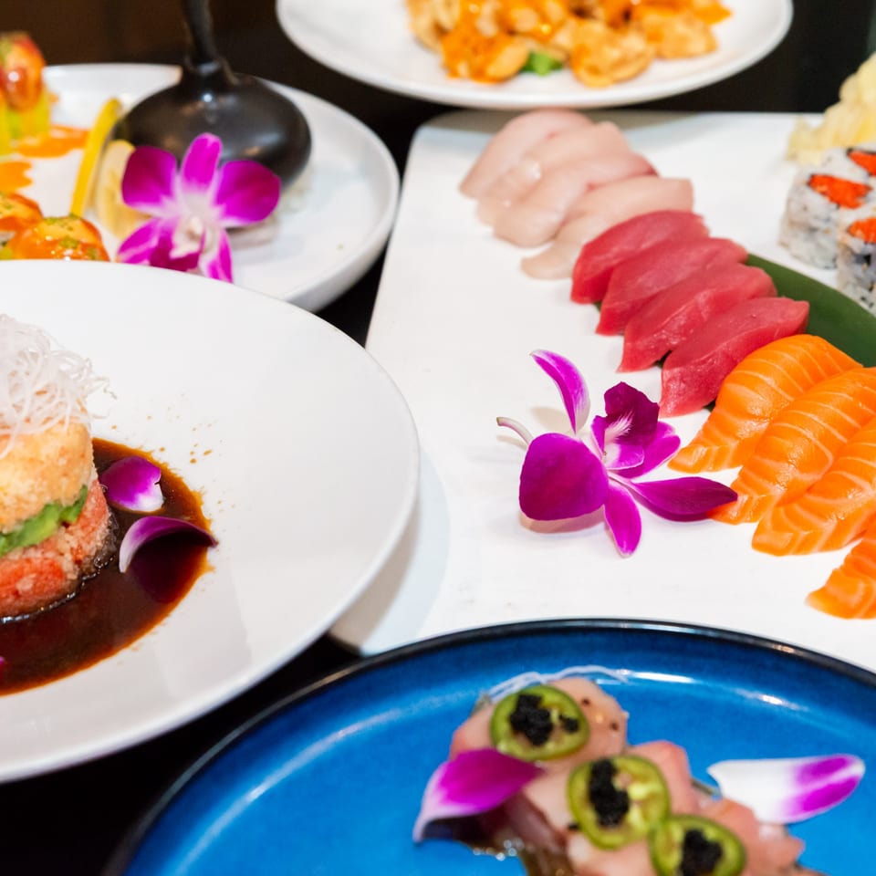 A variety of Japanese dishes, including sushi, sashimi, and a tuna tower, garnished with orchids.