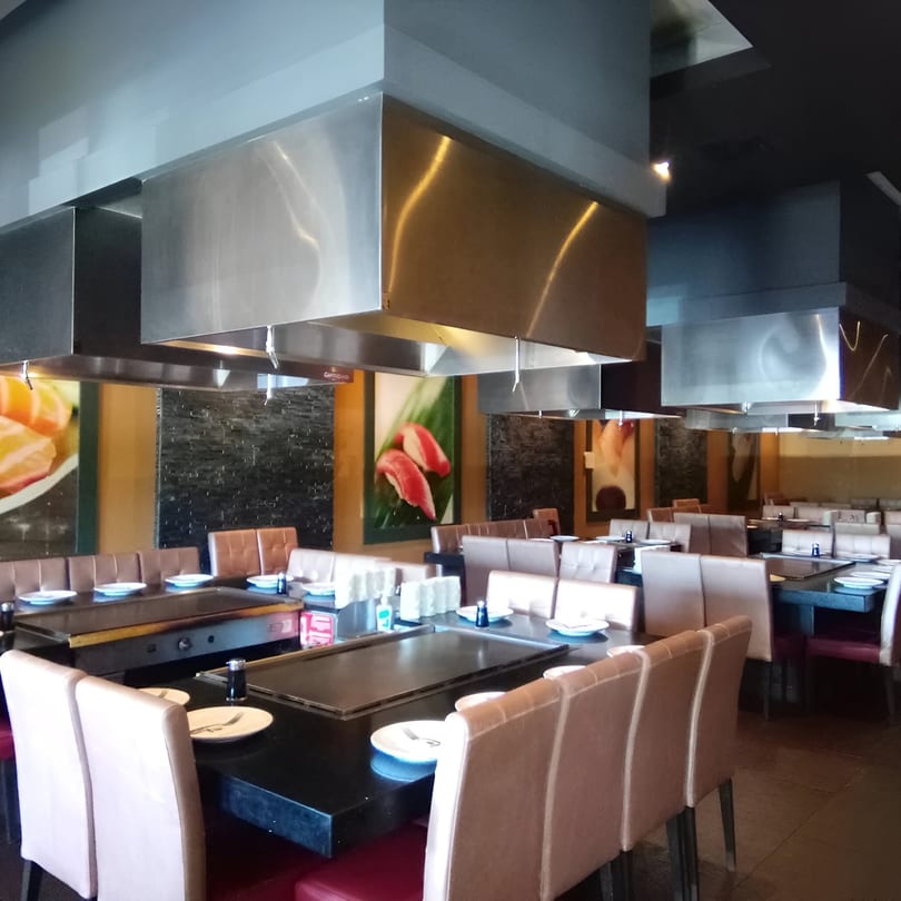 Interior of Wasabi Japanese SteakHouse with multiple hibachi tables and brown chairs under stainless steel hoods.